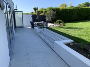 Porcelain patio with matching bluenosed steps, rendered retaining walls, batten screen and millboard decking